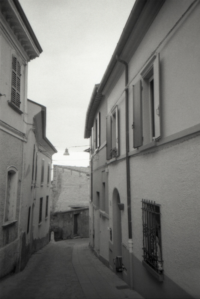 Eine Sicht bergab einer kleinen Straße zwischen zwei Häuserzeilen  in einem Bergdorf in Italien. Zwischen den Häusern sind Straßenlaternen gespannt.