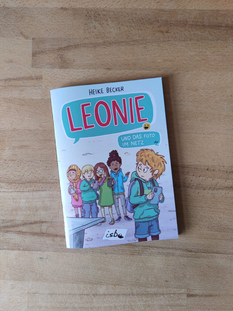 Das Cover von "Leonie und das Foto im Netz": Die Protagonistin Leonie steht im Vordergrund, dahinter eine Gruppe aus viel Mädchen, die Smartphones in der Hand haben, tuscheln und lachen.