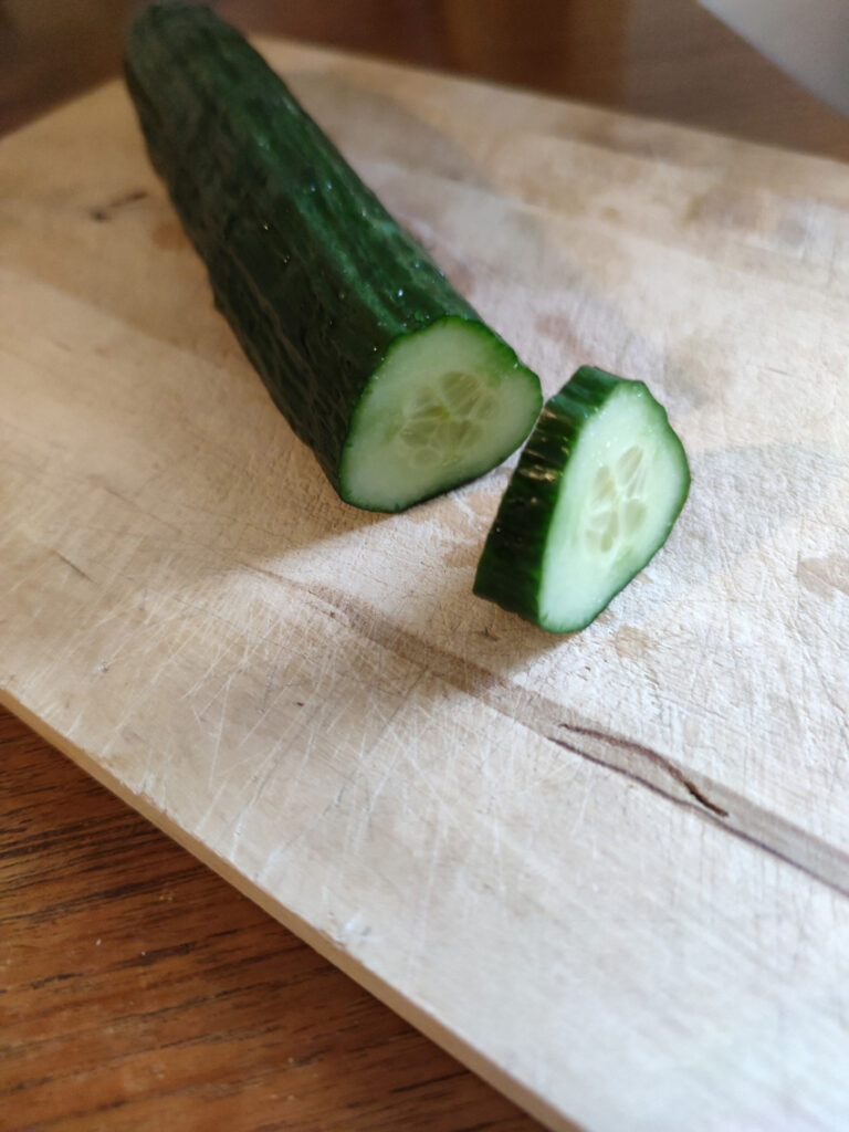 Eine leicht dreickige Gurke auf einem Holzbrett. 